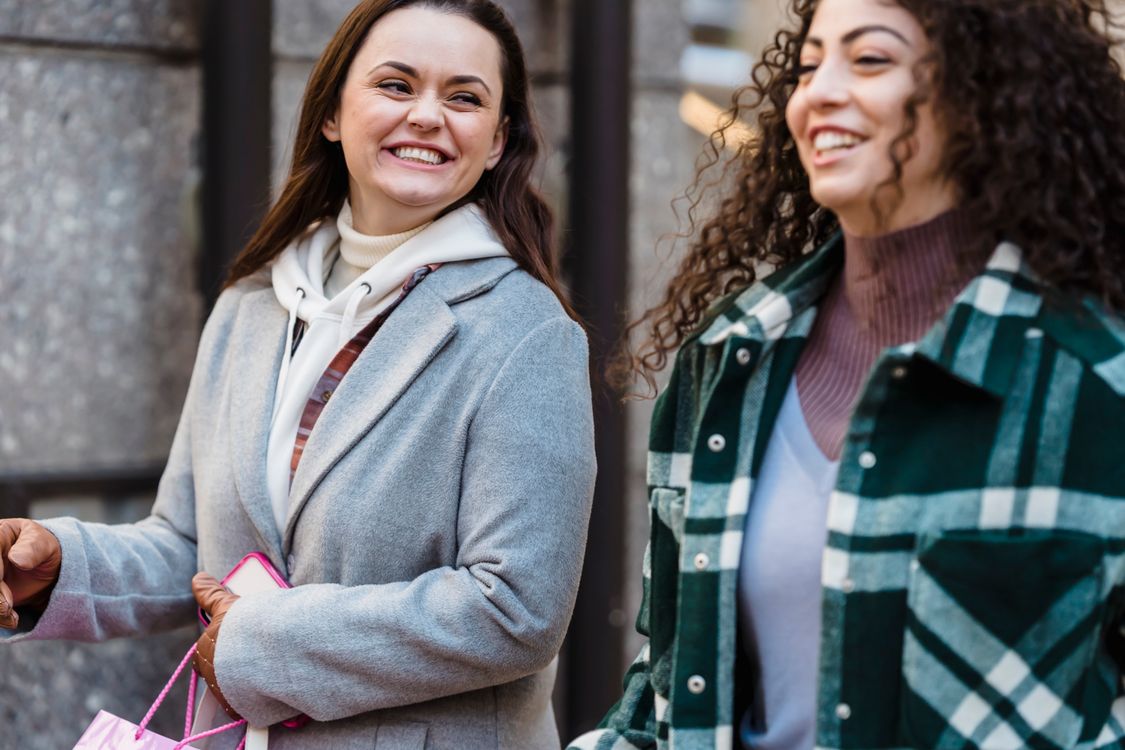 Zwei Freundinnen lachen bei einem Spaziergang durch die Stadt. Lifestylefotografie von Tim Douglas / Pexels.